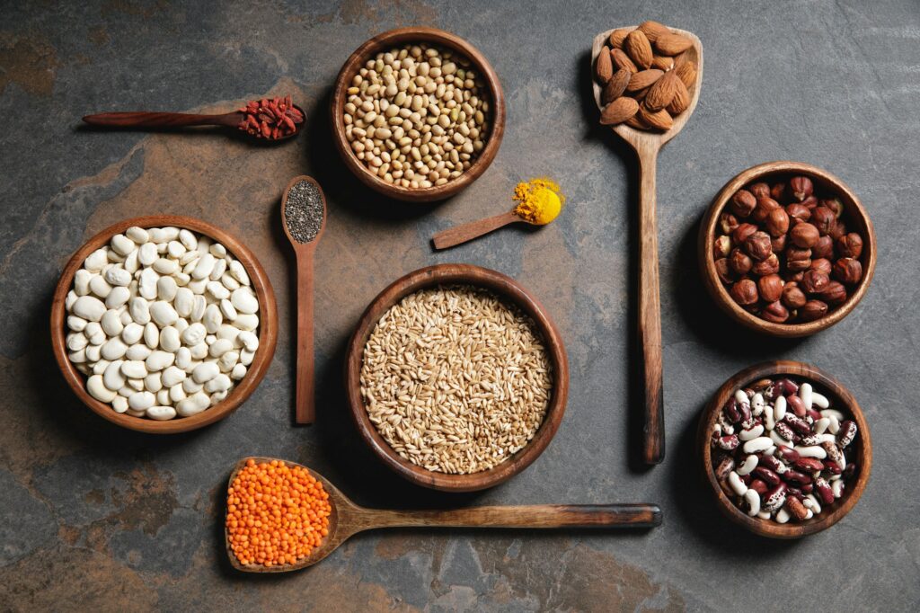 flat lay of wooden bowls and spoons with superfoods, legumes and grains on table